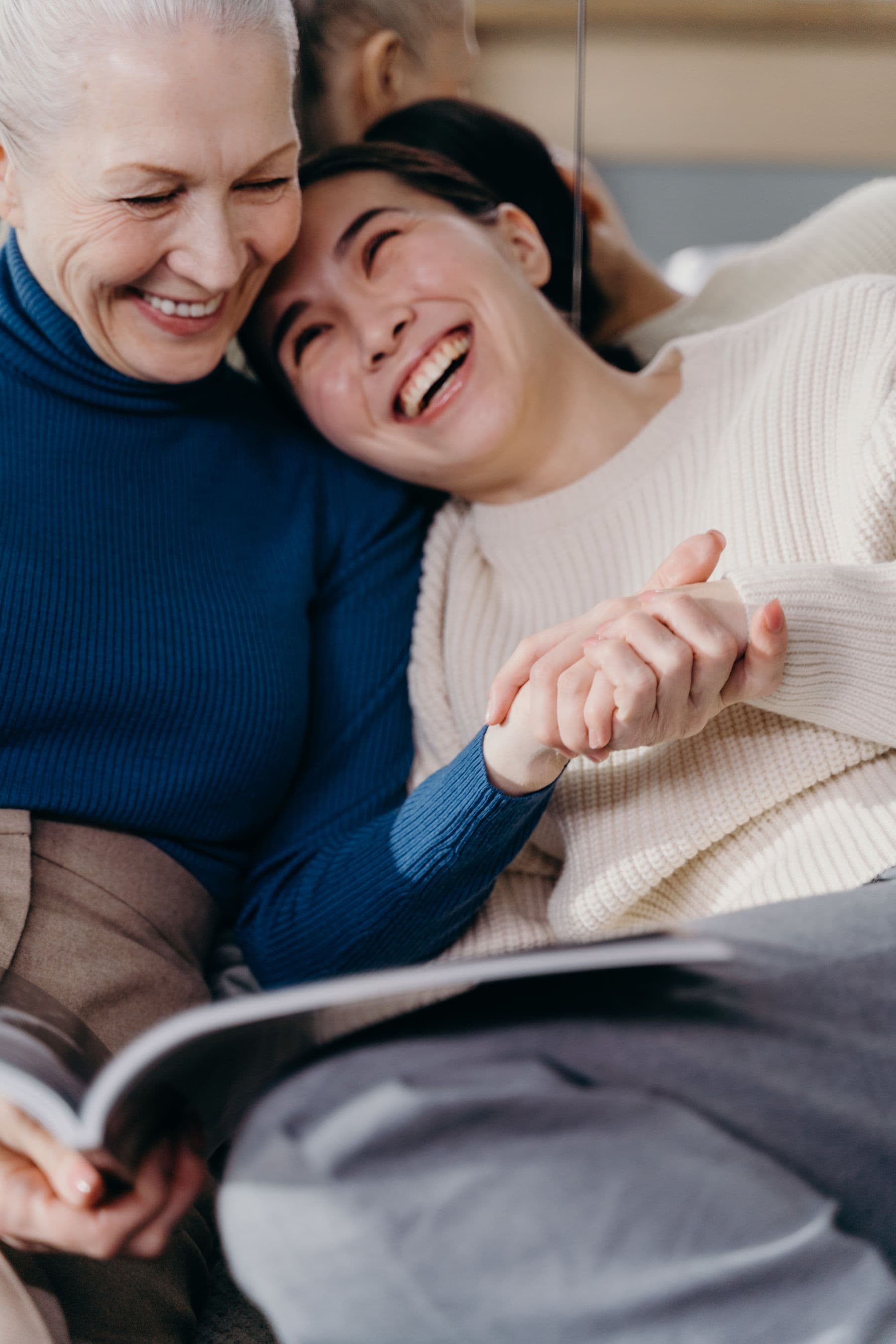 A carer and an older person laughing together at home while looking at a book